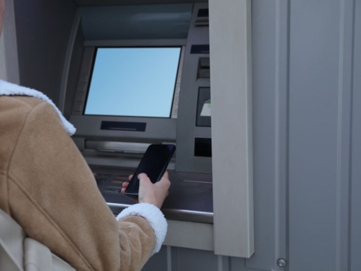 donna con smartphone davanti ad un ATM